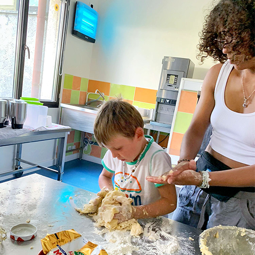 Petit garçon qui cuisine avec une animatrice en colonie de vacances.